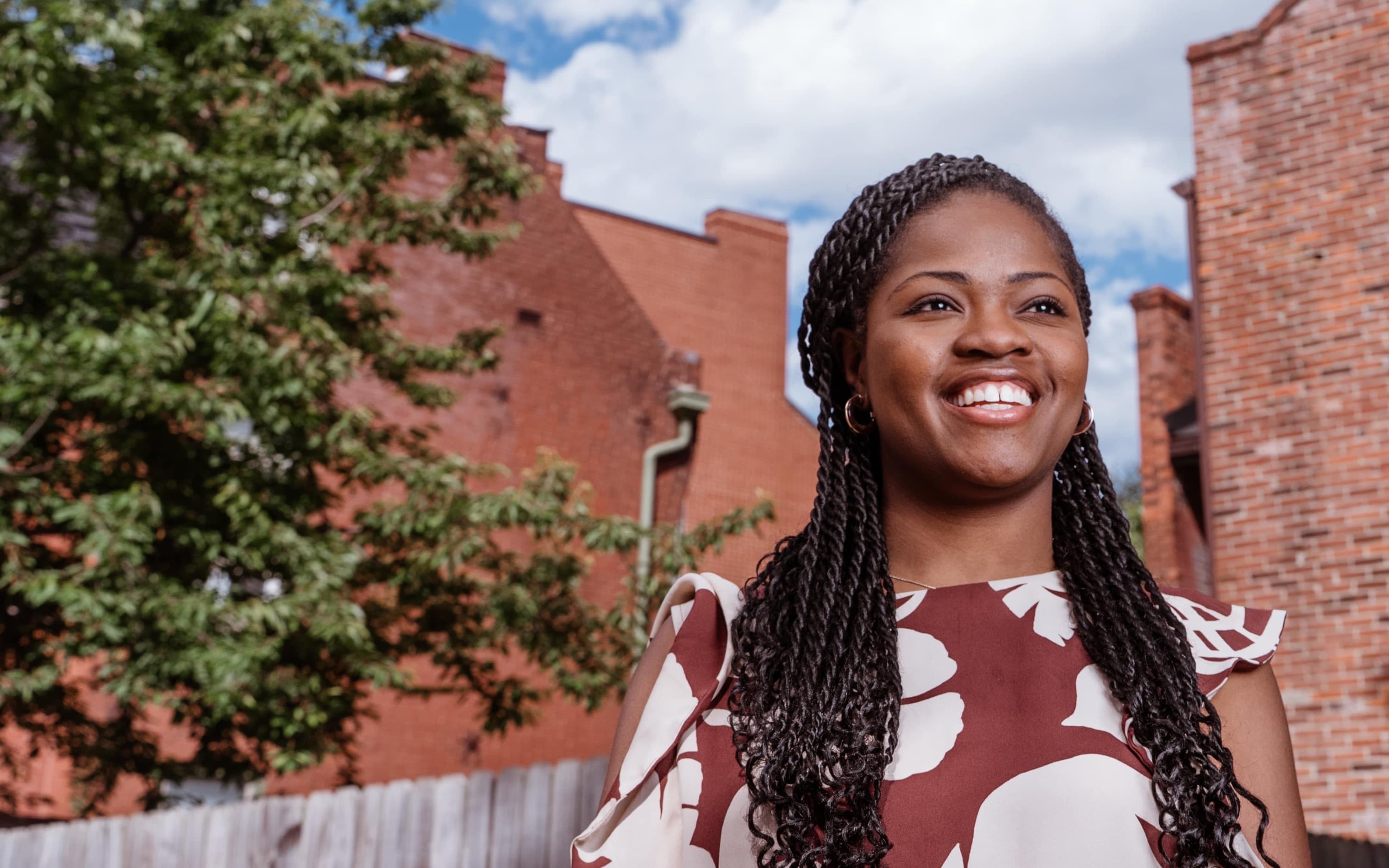 Jami Cox Antwi smiling on a St. Louis street, with brick buildings and a blue sky behind her