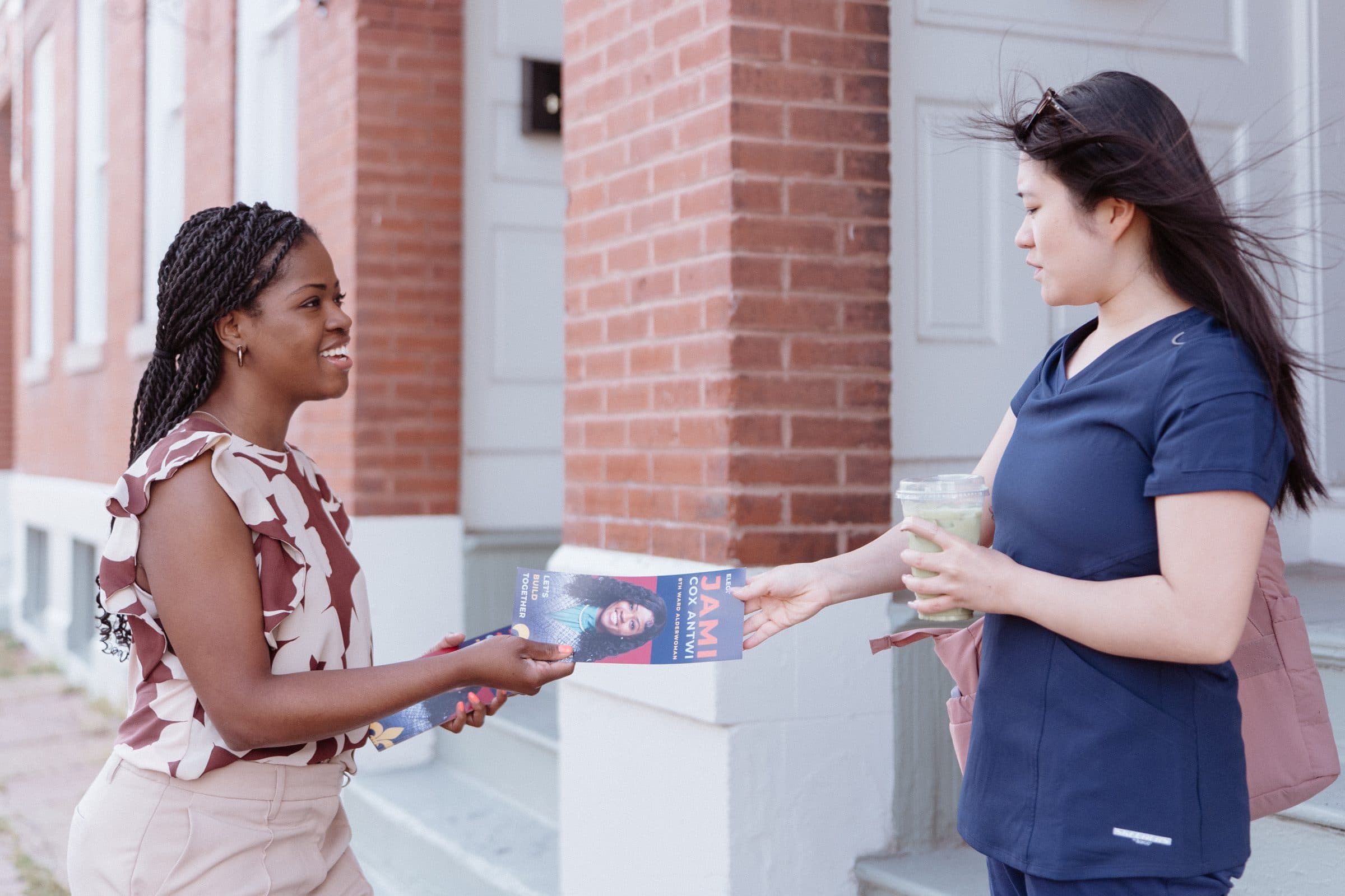 Jami Cox Antwi handing a campaign flyer to a neighbor on a brick-lined street